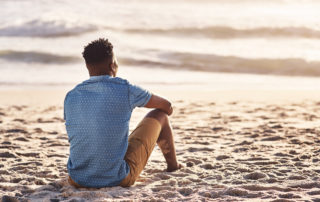 A young man sitting at the water's edge and looking at the view of the ocean