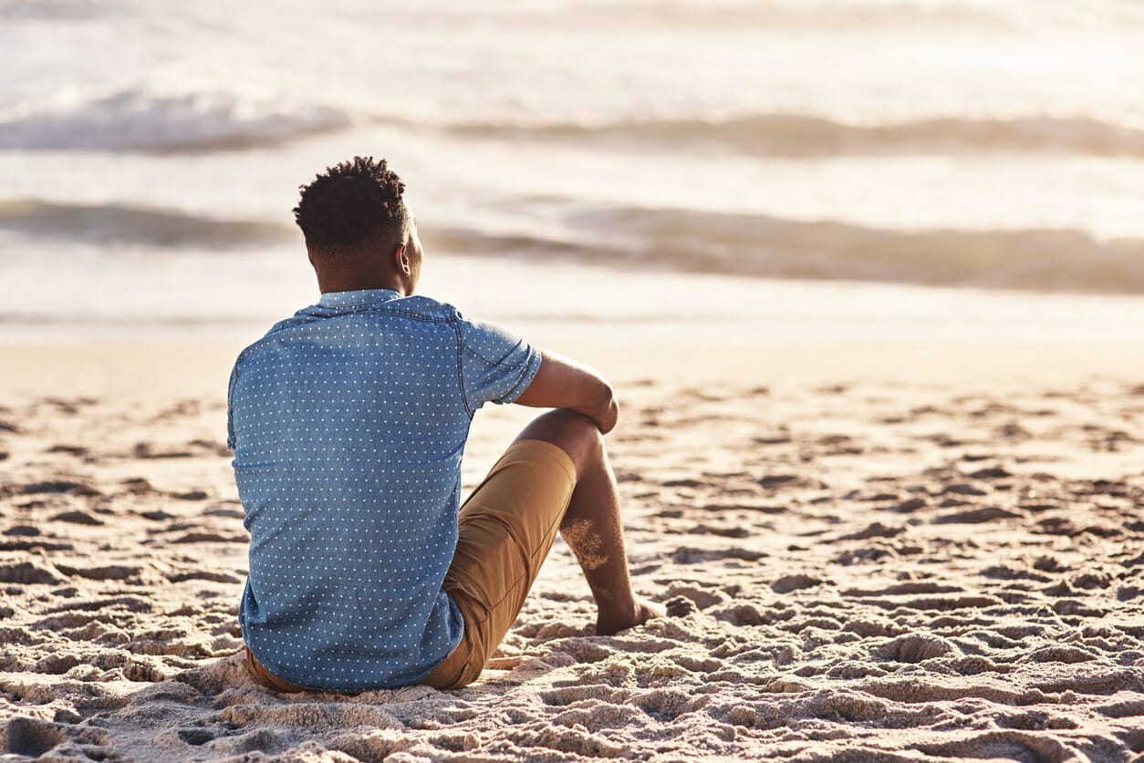 A young man sitting at the water's edge and looking at the view of the ocean
