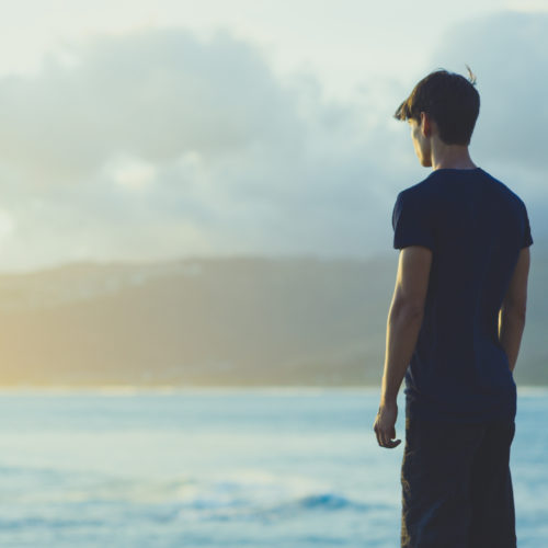 Young man on top ocean cliff during sunset