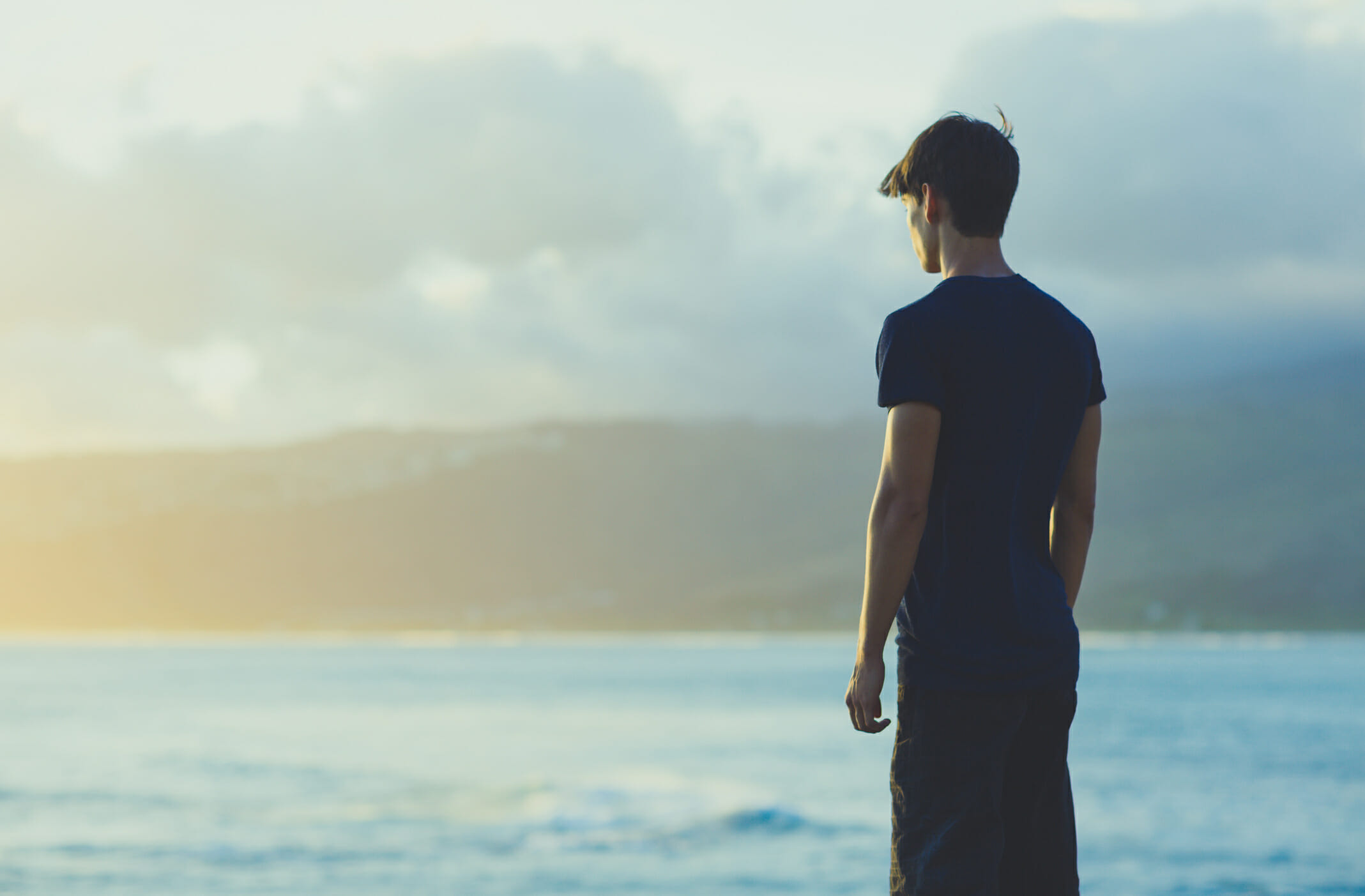 Young man on top ocean cliff during sunset
