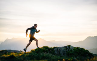 Young man runs on mountain ridge at sunrise
