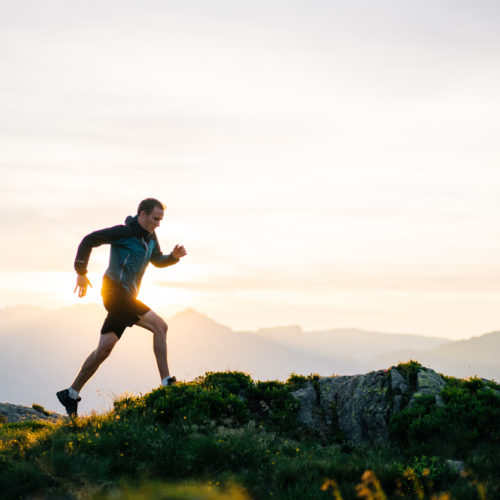 Young man runs on mountain ridge at sunrise