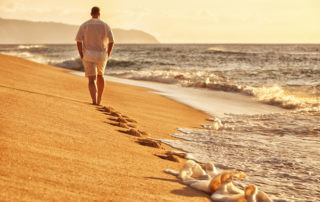 A man walking on a remote beach at sunrise.