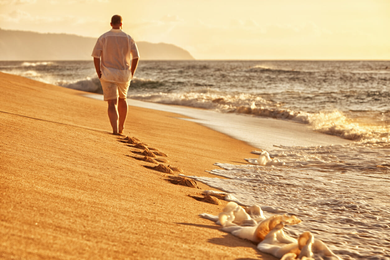 A man walking on a remote beach at sunrise.