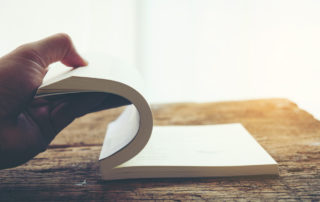 Hand open turning next page of old book at a wooden table