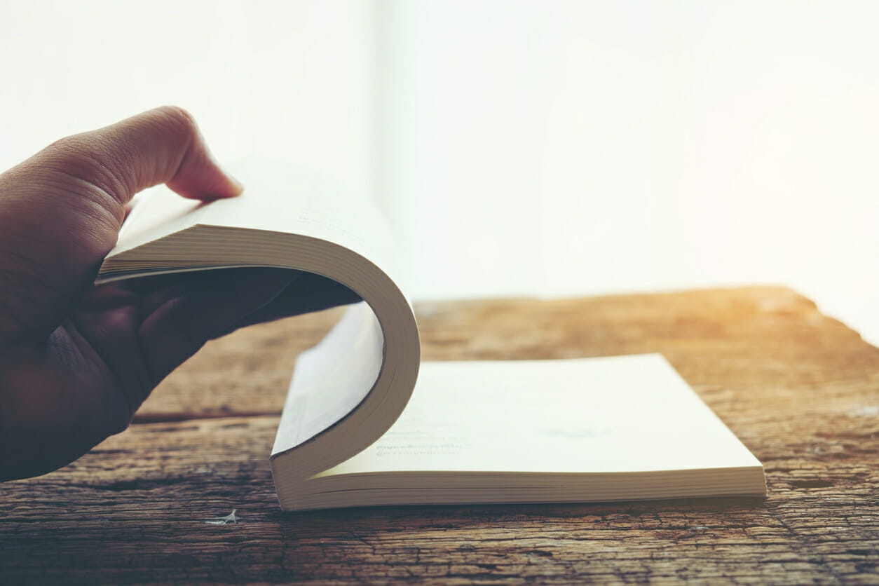 Hand open turning next page of old book at a wooden table