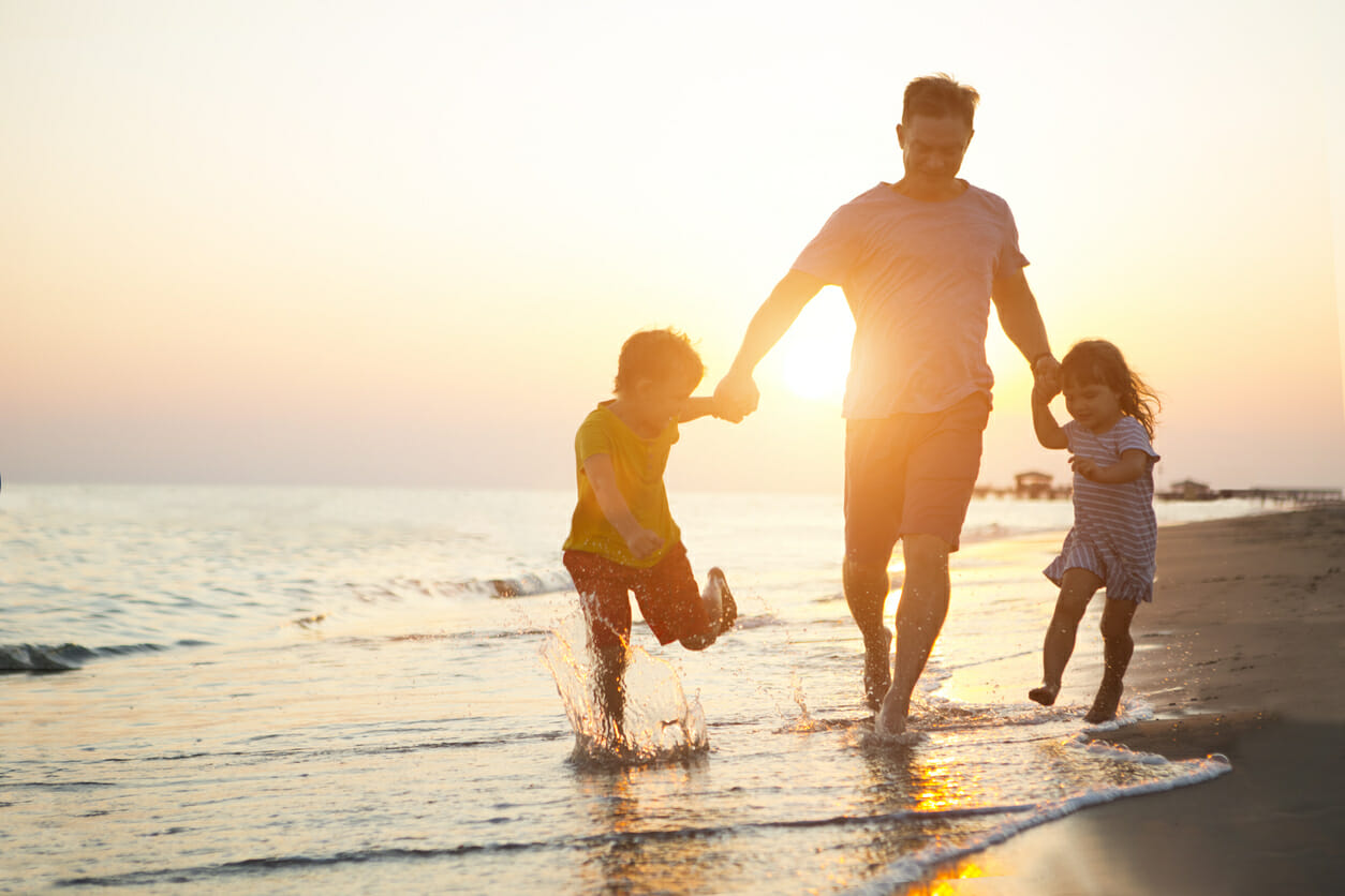 Happy father and two children playing on the beach.