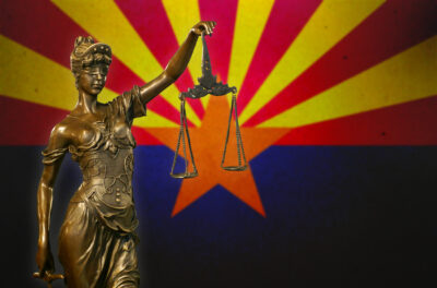 Close-up of a small bronze statuette of Lady Justice before a flag of Arizona.