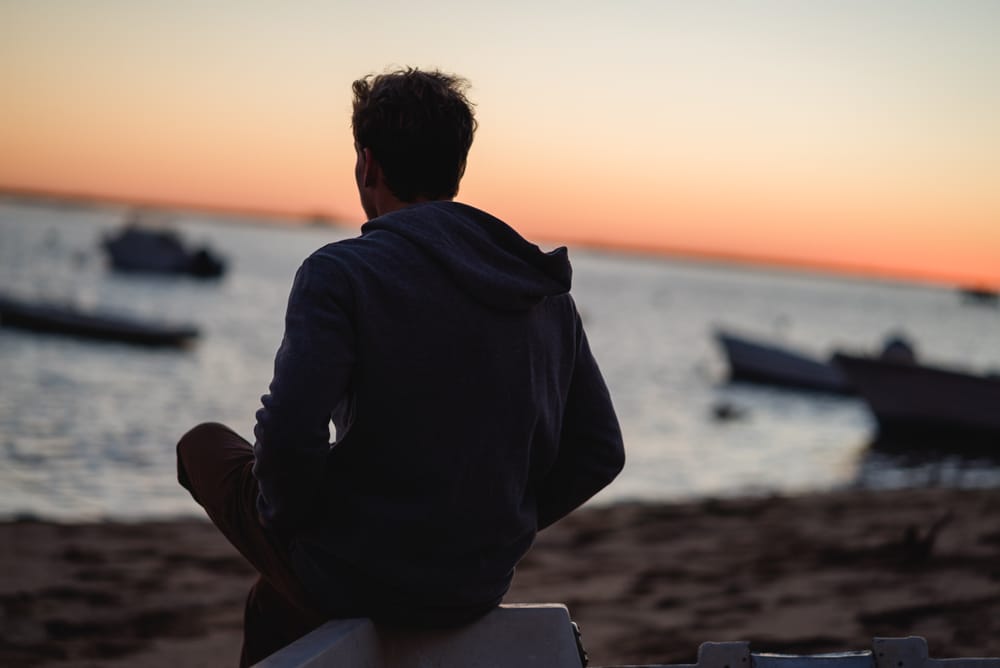 Young man sits on a beach.